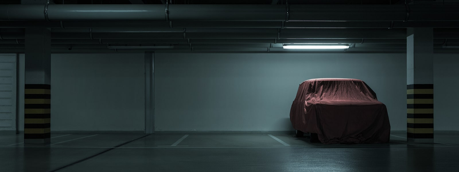 Long-Term Storage: Red covered vintage car in empty underground parking